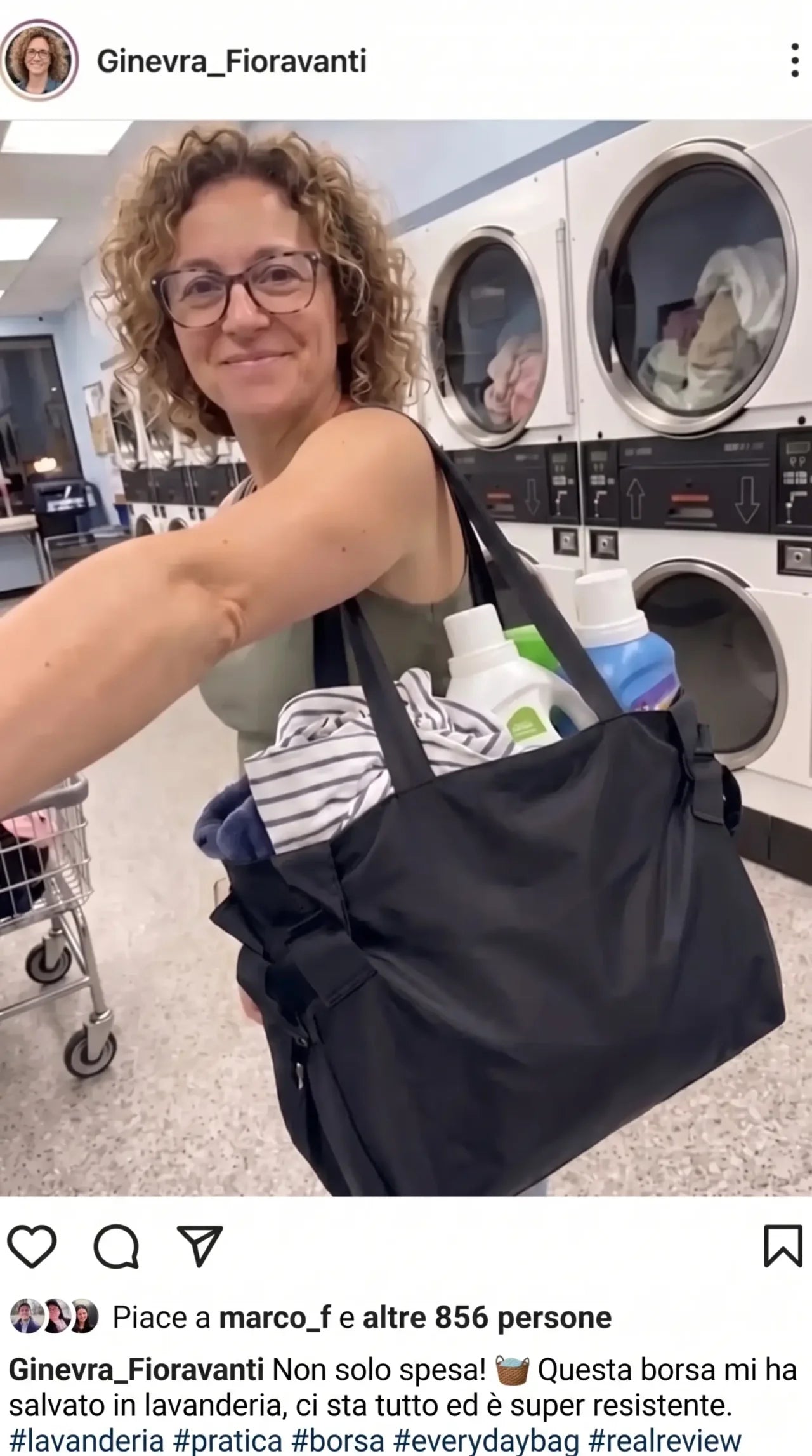 Cliente in lavanderia con la Colette Bag nera piena di panni e flaconi di detersivo